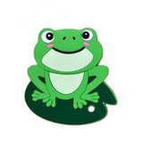 A green silicone teether in the shape of a smiling frog with a lily pad background.