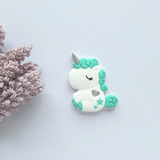A collection of unicorn-shaped silicone teethers in various colors, including pink, blue, green, and purple, designed to be used by infants.