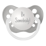 A gray orthodontic pacifier with a silicone nipple that is engraved with the text "Be Somebody!"