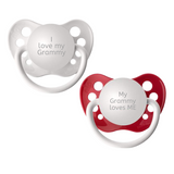 Two orthodontic pacifiers, one white and one red, each with an engraved message stating 'I love my GRAMMY' and 'MY GRAMMY LOVES ME'.