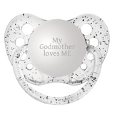 A clear silicone orthodontic pacifier with 'MY GODMOTHER LOVES ME' engraved on the pacifier