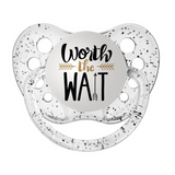 A clear silicone pacifier with 'WORTH THE WAIT' engraved on the front, along with a small decorative heart and arrow symbol.